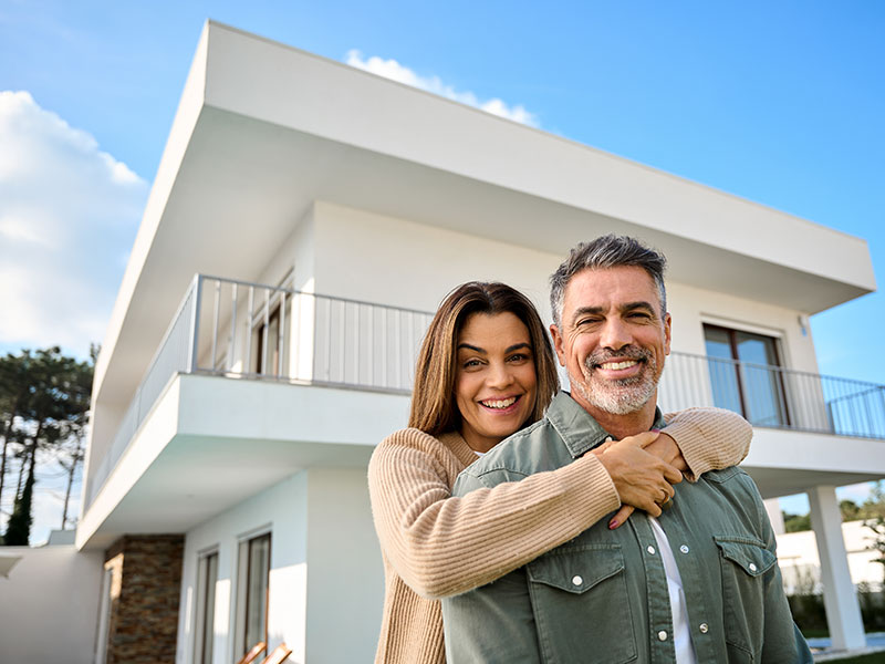 Unsere Immobilien für Käufer/innen EIn zufriedenes Paar umarmt sich vor der neuen, eigenen Immobilie