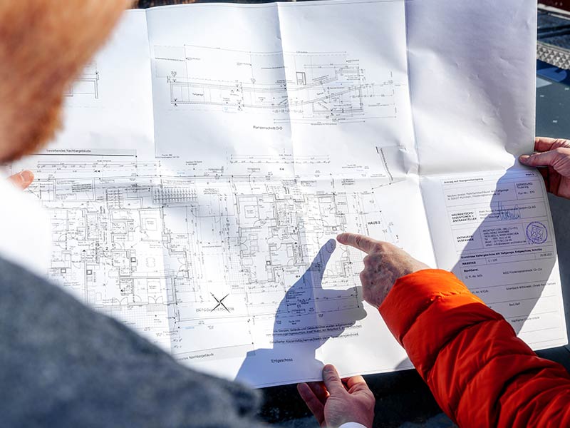 Mitarbeiter von Heim und Leben München mit Bauplan und Kunde bei der Baustellenbegehung